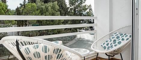 A balcony with two white wicker chairs and a small table.