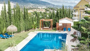 A swimming pool with lounge chairs, a wooden pergola, and a view of a cityscape and mountains in the background. - GO- Golden Banus by Roomservices (Marbella)
