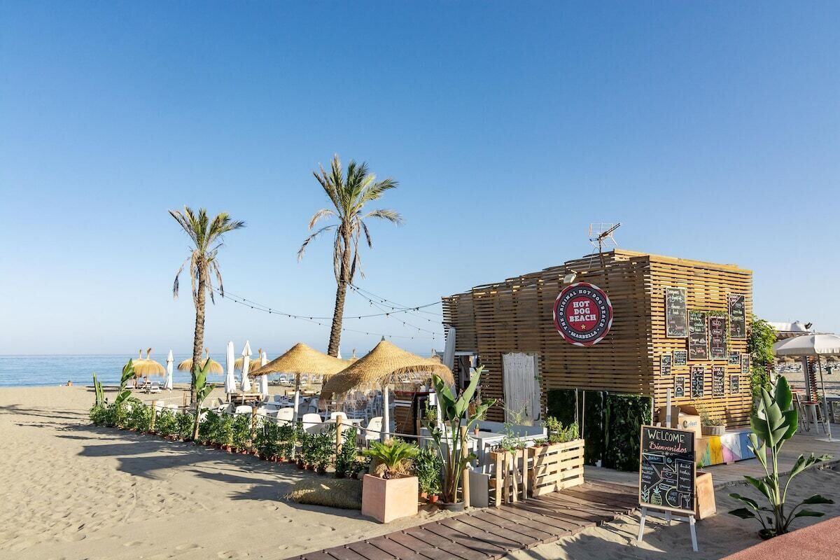 Un restaurant situé en bord de mer, avec une façade en bois, des palmiers et des parasols en chaume.
