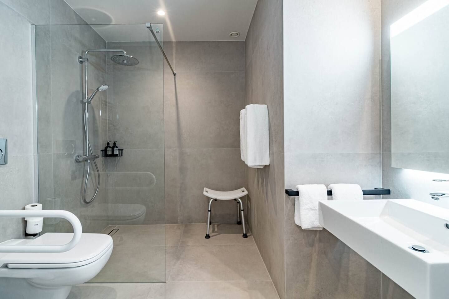 A modern bathroom with a glass-enclosed shower, a white toilet, a sink, and a small white stool.