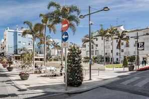 A street with a no entry sign, a directional sign, and a parking sign. There are palm trees, a flower bed, and buildings in the background. - A6- Seaclub Suites by Roomservices (Estepona)