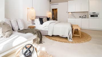 A modern bedroom with a bed, bedside tables, a wooden bench, and a kitchen area with cabinets and appliances.
