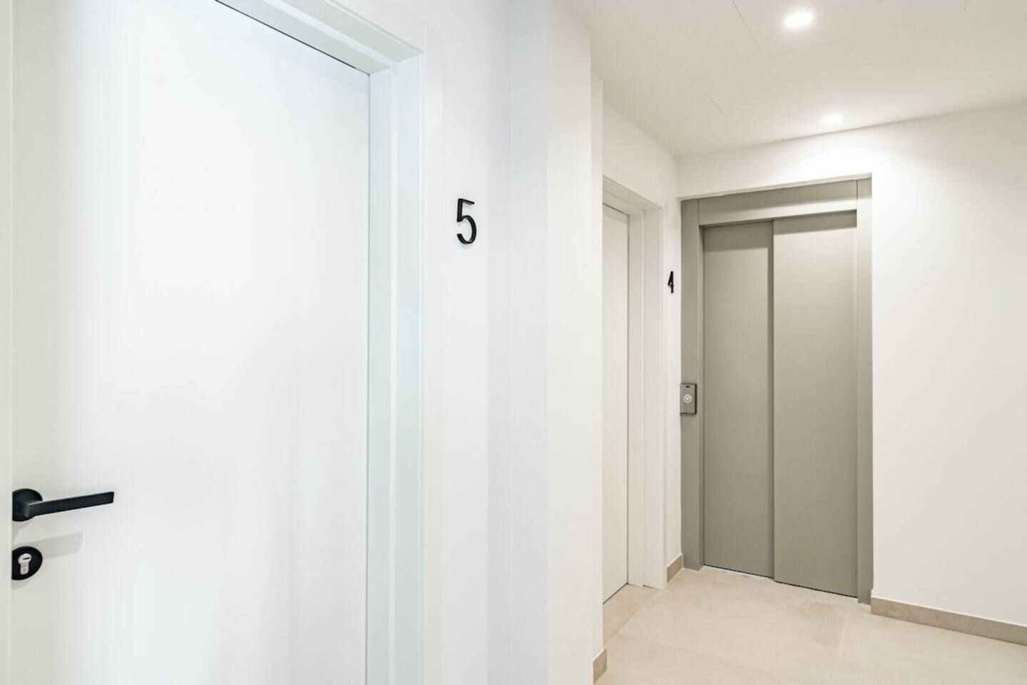 Un pasillo con una puerta numerada 5, un ascensor y una puerta numerada 4.