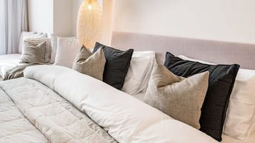 Una cama bien hecha con cubrecama acolchada, varios almohadones en diferentes tonos y una lámpara colgante arriba.