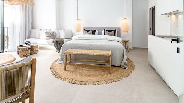 Ein modernes Schlafzimmer mit einem großen Bett, Nachttischen, einer Bank und einer Essecke mit Stuhl und Tisch.