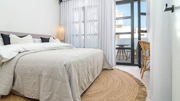 Een slaapkamer met een bed, een rond geweven vloerkleed, een stoel en uitzicht door een glazen deur.