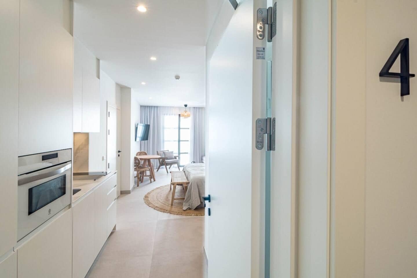 A modern kitchen with built-in appliances, a dining area with a round table, and a bedroom with a bed and a TV.