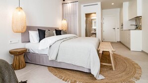 A modern bedroom with a large bed, bedside tables, a round woven rug, and a small wooden stool. - A4- Seaclub Suites by Roomservices (Estepona)