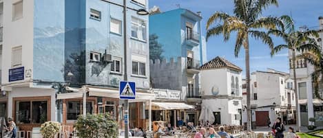 A street with outdoor seating, a pedestrian crossing sign, and palm trees.