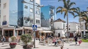 A street scene with outdoor seating, palm trees, and buildings with balconies. - A4- Seaclub Suites by Roomservices (Estepona)
