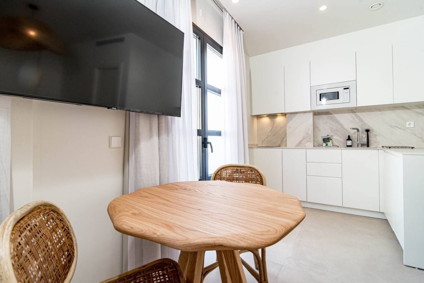 A modern kitchen with white cabinets, a built-in microwave, and a dining area with a wooden table and wicker chairs.
