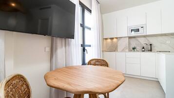 A modern kitchen with white cabinets, a built-in microwave, and a dining area with a wooden table and wicker chairs.