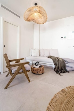 A modern living room with a white sofa, a wooden chair, a round wooden coffee table, and a woven light fixture. - Seaclub Suites by Roomservices (Estepona)