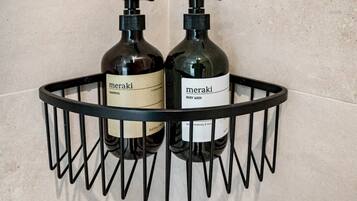 Estante de metal negro con dos botellas de jabón corporal y champú Meraki.