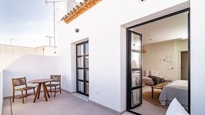 A modern outdoor patio with a table and chairs, a sliding glass door leading to a bedroom with a bed and a sofa. - Seaclub Suites by Roomservices (Estepona)