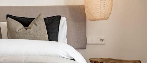 A bedroom with a bed, pillows, a hanging light fixture, and a wooden stool.
