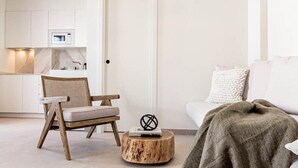 A modern living room with a white sofa, a wooden chair, a round wooden table, and a woven hanging light fixture. - Seaclub Suites by Roomservices (Estepona)