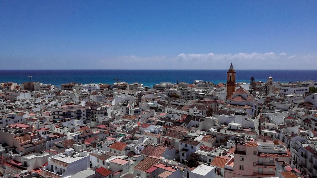A coastal cityscape with dense urban buildings, a prominent tower, and a clear view of the sea.