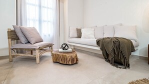A modern living room with a wooden chair, a round wooden table, a white sofa, and a window with sheer curtains. - A1- Seaclub Suites by Roomservices (Estepona)