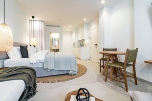 A modern hotel room with a bed, bedside table, chair, and a small dining area with a table and chairs. - A1- Seaclub Suites by Roomservices (Estepona)