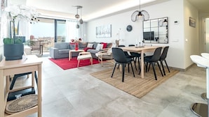 A modern living room with a sofa, dining table, and chairs. There is a large window providing a view of the city. - Inf46p - Spacious Holiday Home in Estepona (Estepona)
