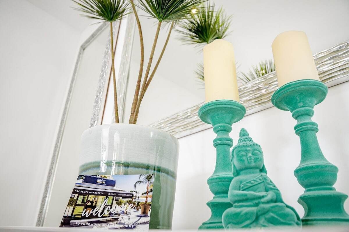 A clear glass vase with a printed label, two teal candle holders, and a decorative Buddha statue.