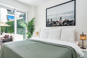 A modern bedroom with a bed, a large window, a potted plant, and a framed picture on the wall. - Lcr1- Lovely Ground Floor Apartment, Puerto Banus (Marbella)