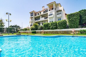 A swimming pool with a clear blue water surface, surrounded by a stone wall and lush greenery. - Lcr1- Lovely Ground Floor Apartment, Puerto Banus (Marbella)