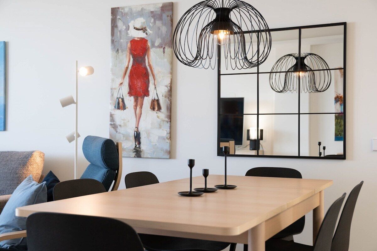 Un espace de repas moderne avec une table en bois, des chaises noires, un grand tableau abstrait, un lampadaire et un miroir avec un cadre noir.