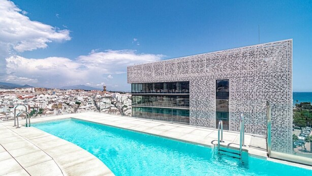 Un edificio moderno con una fachada de azulejos únicos, una piscina y vistas a un pueblo costero.