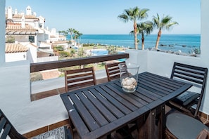 Un balcón con mesa y sillas de madera, con vista a una piscina y una playa.