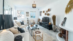 A modern living room with a sofa, coffee table, and TV. There are decorative items on the walls and a fireplace. - PL - Beachfront Seaview Aptm - Playa de la Lucera (Mijas)