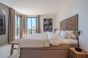 A bedroom with a large bed, a wooden bench, a nightstand with a lamp, and a view of the outdoors. - Jdg7-stunning Holiday Home 100 Meters From Beach (Marbella)
