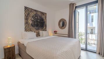 Quarto com cama grande, uma obra de arte na parede, espelho redondo e vista para o exterior.