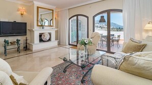 Amplia sala de estar con televisor grande, chimenea, mesa de centro de vidrio y vistas al exterior.