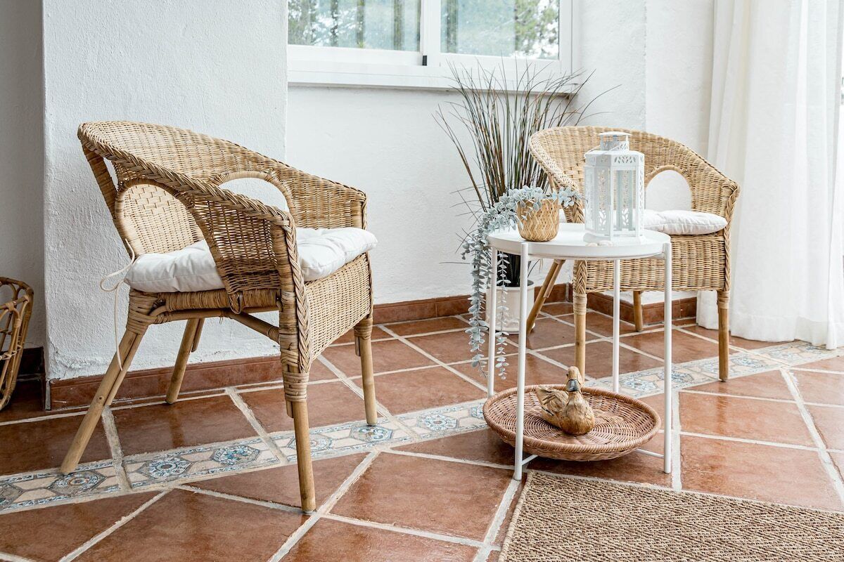 Ein Zimmer mit zwei Korbstühlen, einem kleinen weißen Tisch und einer dekorativen Vase.
