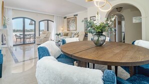 Un salón amplio con una mesa redonda de madera, sillas tapizadas en azul y un sofá blanco y mullido.