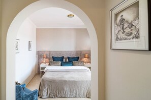 Une chambre à coucher comprenant un lit, deux tables de chevet, une tête de lit et une œuvre d’art encadrée accrochée au mur.