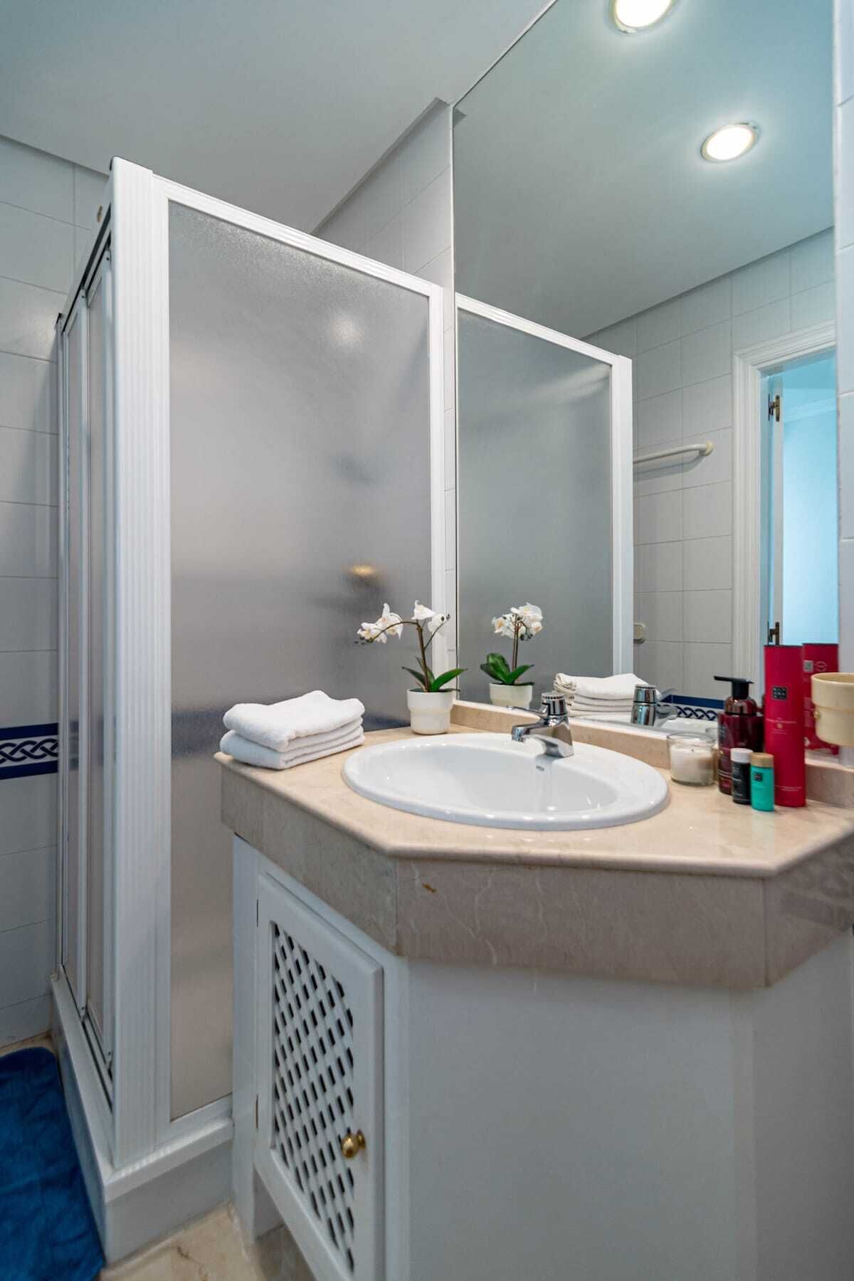 Un baño con lavamanos blanco, un espejo y cabina de ducha.
