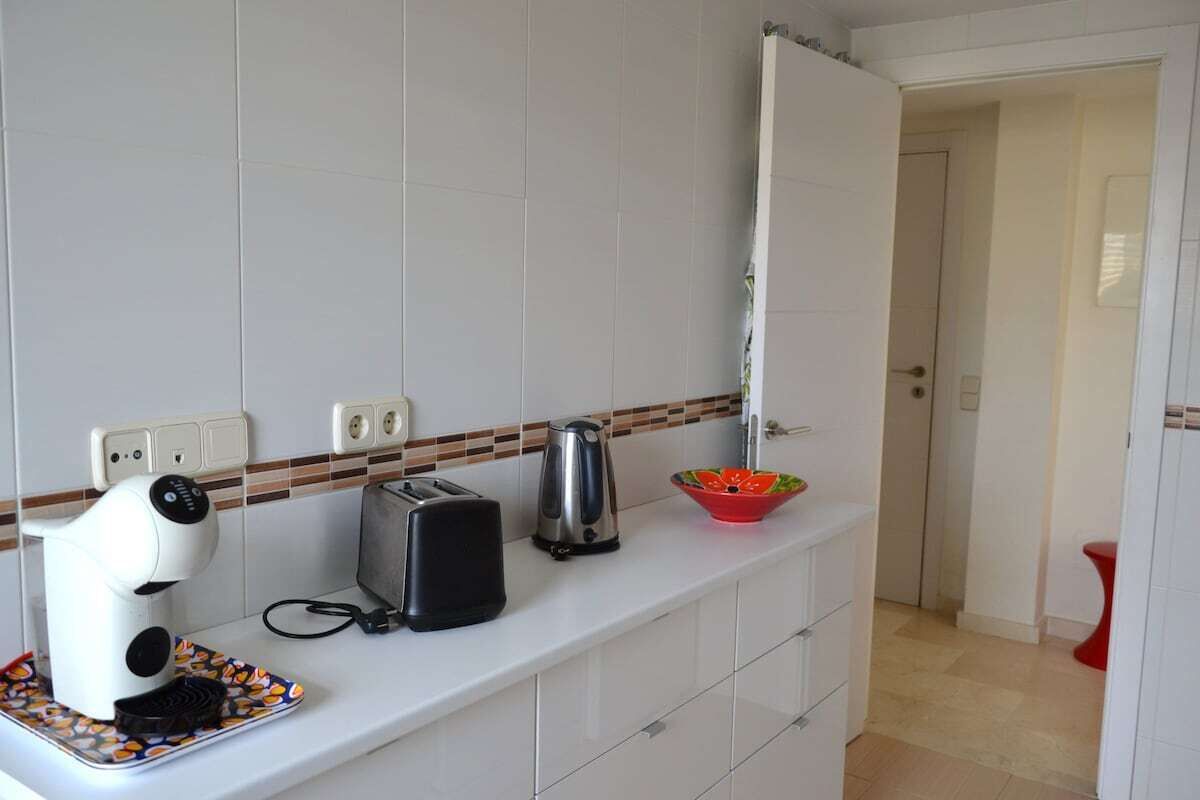 Una cocina con armarios blancos, un tostador, una tetera y un cuenco de fruta sobre la encimera.