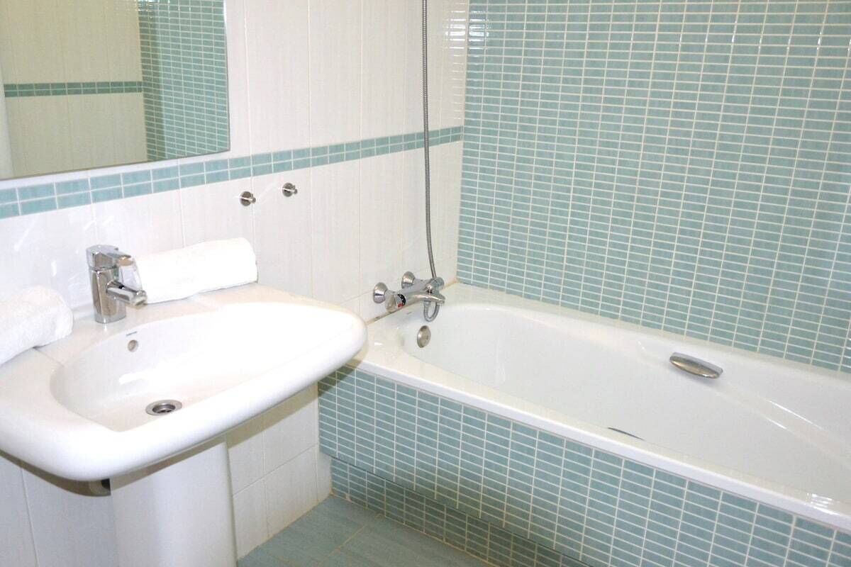 A bathroom with a white sink, a bathtub, and blue-tiled walls.