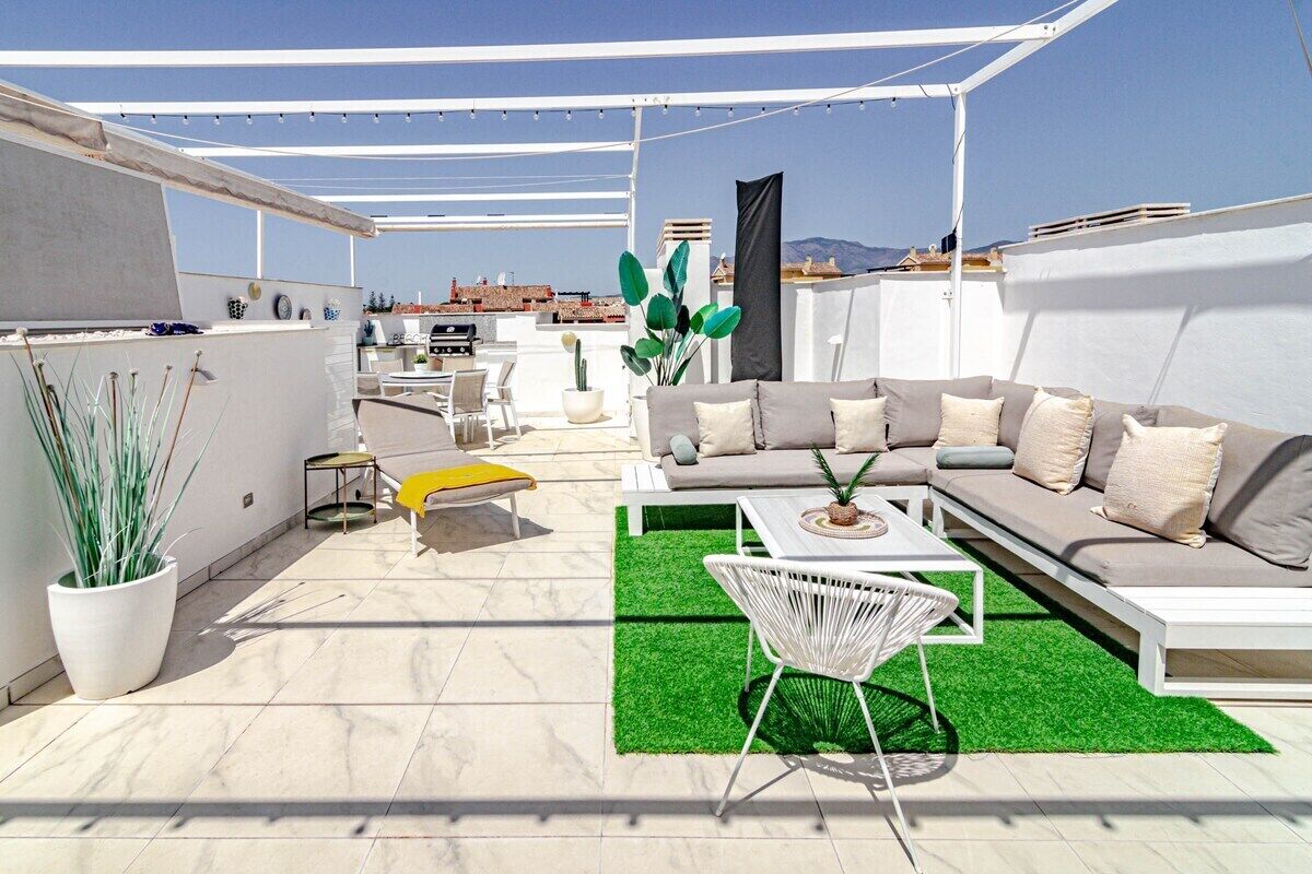 A rooftop patio with a sofa, chairs, a small table, and potted plants.