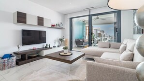 Un soggiorno moderno con una grande TV a schermo piatto, un tavolino, un divano e una porta-vetrata scorrevole che dà su un balcone.