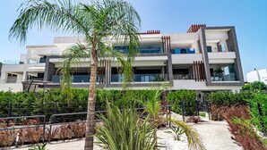 Un edificio moderno a più piani con balconi, immerso nel verde e circondato da palme.