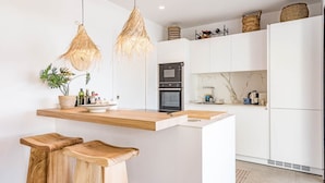 Una cocina moderna con una isla central, taburetes de madera, horno empotrado y refrigerador.