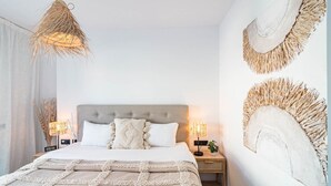 Un dormitorio con una cama grande, dos mesitas de noche, una lámpara colgante y cuadros en la pared.