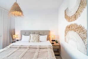 Quarto com uma cama grande, duas mesas de cabeceira, luminária pendente e decoração na parede.