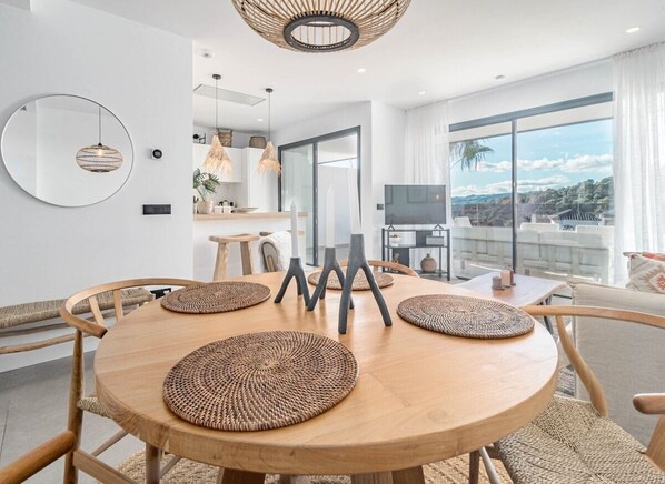 Uma área de jantar moderna com mesa redonda de madeira, jogos americanos trançados e luminária pendente.
