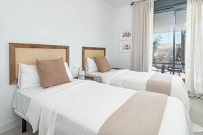 Habitación de hotel con dos camas, un ventanal con cortinas y un balcón.