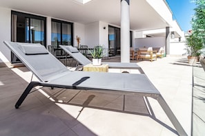 A modern outdoor lounge area with sun loungers, a table with chairs, and potted plants. - Lme4bb Sb4bb- Apotel las Mesas by Roomservices (Estepona)